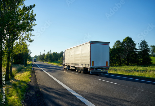 Two trucks going against each other on an asphalt road lined with deciduous trees