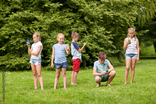 kids with smartphones playing game in summer park