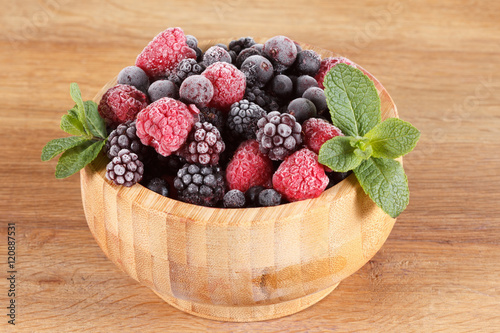 Frozen berries in wooden bowl, covered with ice photo