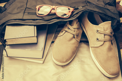 Top view of casual life style bag ; Old book,notebook,red glasses and casual shoes from inside bag.In Vintage tone