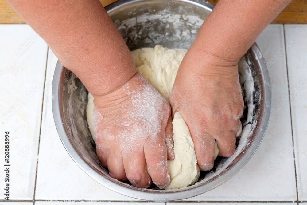 Woman's hands knead dough on a metal bowl