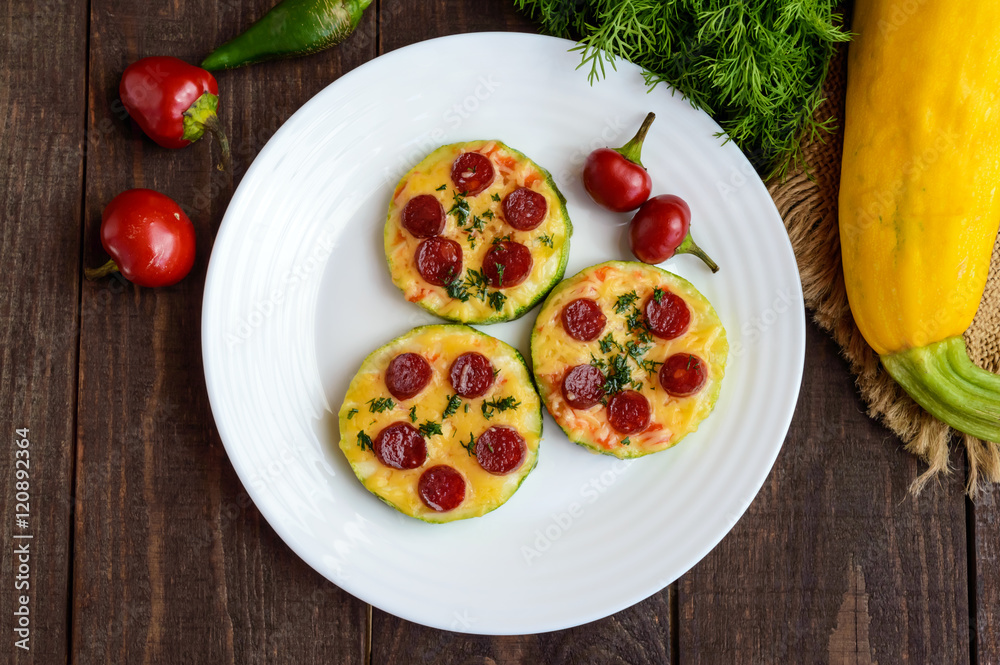 Small zucchini pizza on the circles with pepperoni and mozzarella. On a dark wooden background.