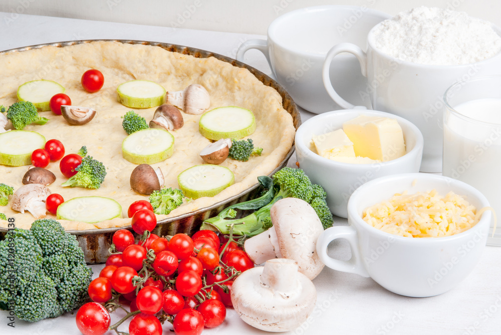 The selection of ingredients for the preparation of traditional French dishes quiche lorraine, on white wooden table with a baked dough in the baking dish in the cooking process, close view The selection of ingredients for the preparation of traditional French dishes quiche lorraine, on white wooden table with a baked dough in the baking dish in the cooking process, close view