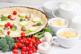 The selection of ingredients for the preparation of traditional French dishes quiche lorraine, on white wooden table with a baked dough in the baking dish in the cooking process, close view