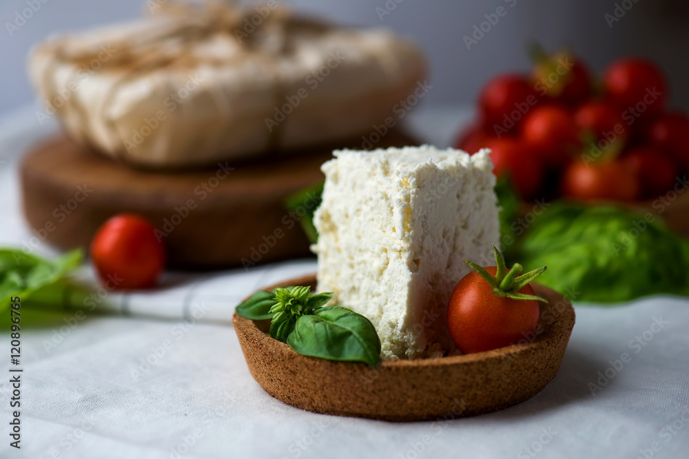 Homemade ricotta cheese with cherry-tomatoes and basil leaves in cork saucer Homemade ricotta cheese with cherry-tomatoes and basil leaves in cork saucer