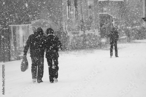 Snowing urban landscape with people passing by