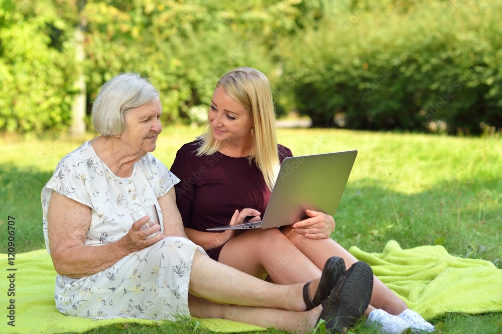 Young woman helping an elderly use the laptop in the park.