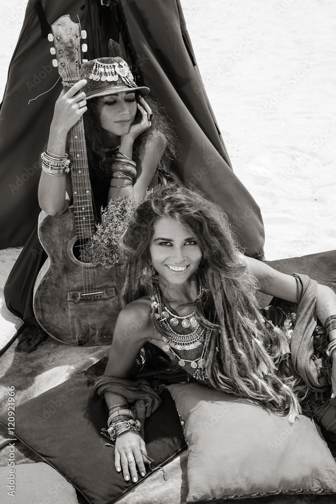 Two beautiful gypsy girls with guitar on pillows at tepee