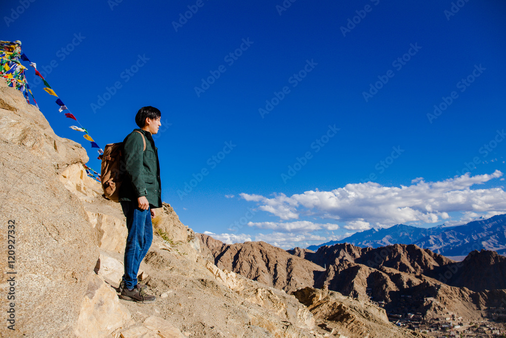 Young Asian traveler standing on high hills and looking away at the village over blue sky background in Leh, Ladakh, India
