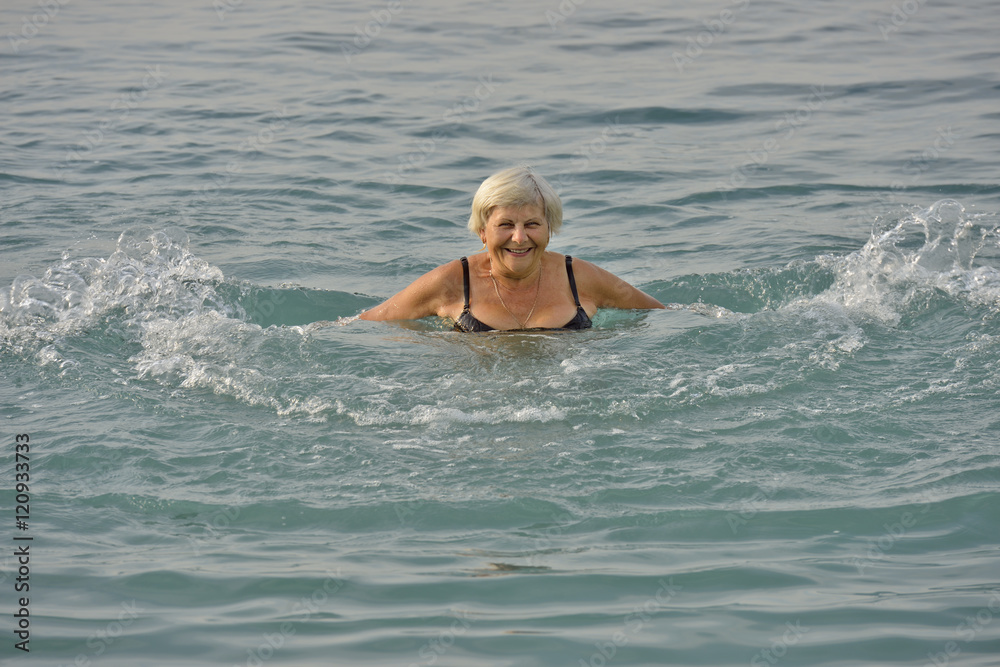 Aged woman is doing motions in light clear sea water.
