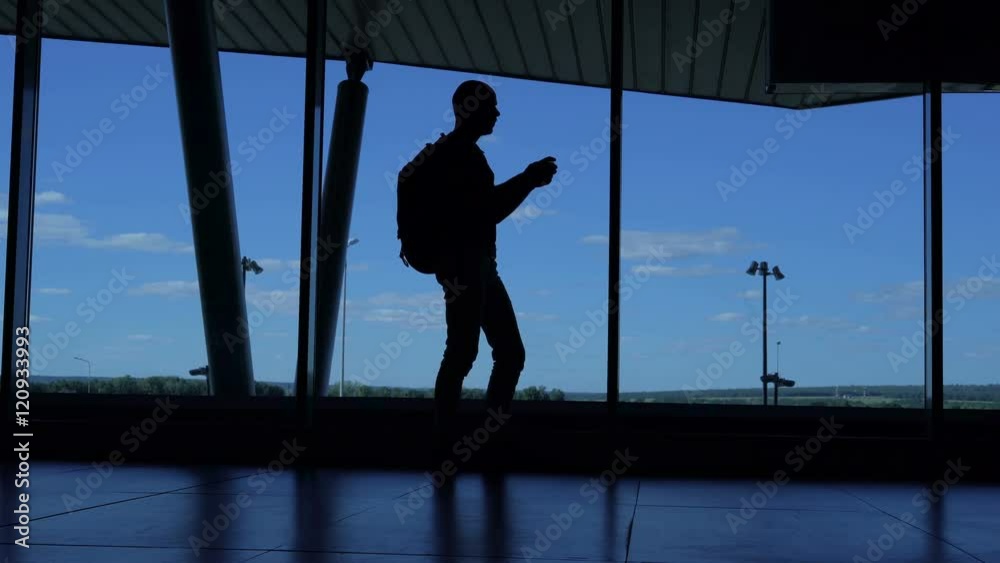 Young man with a backpack standing in an airport lounge and enjoy your smartphone. Young man with a backpack standing in an airport lounge and enjoy your smartphone.