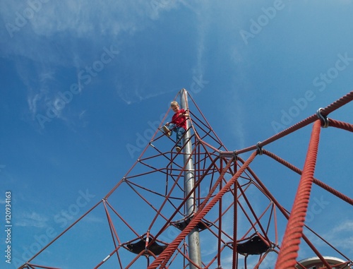 Boy on the top of pyramid net climber under blue sky with white clouds