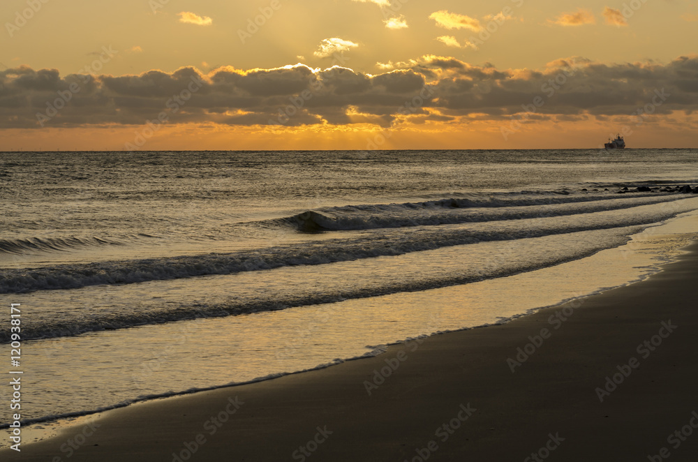 Obraz premium Sea-going vessel near the coast at sunset.