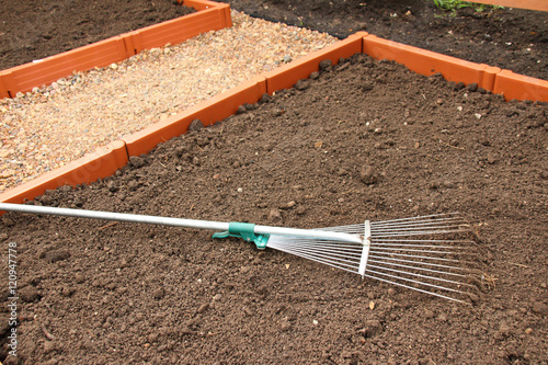 Soil alignment with a lawn rake on a modern plastic raised garden vegetable bed in the summer garden © argot