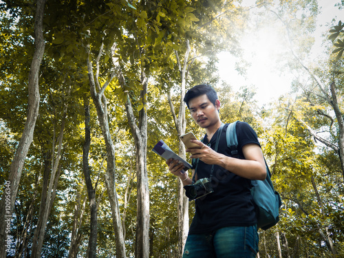 A man backpack trying to find their way. Frustrated young man examining map leaning at forest. and sun light on above in spring season