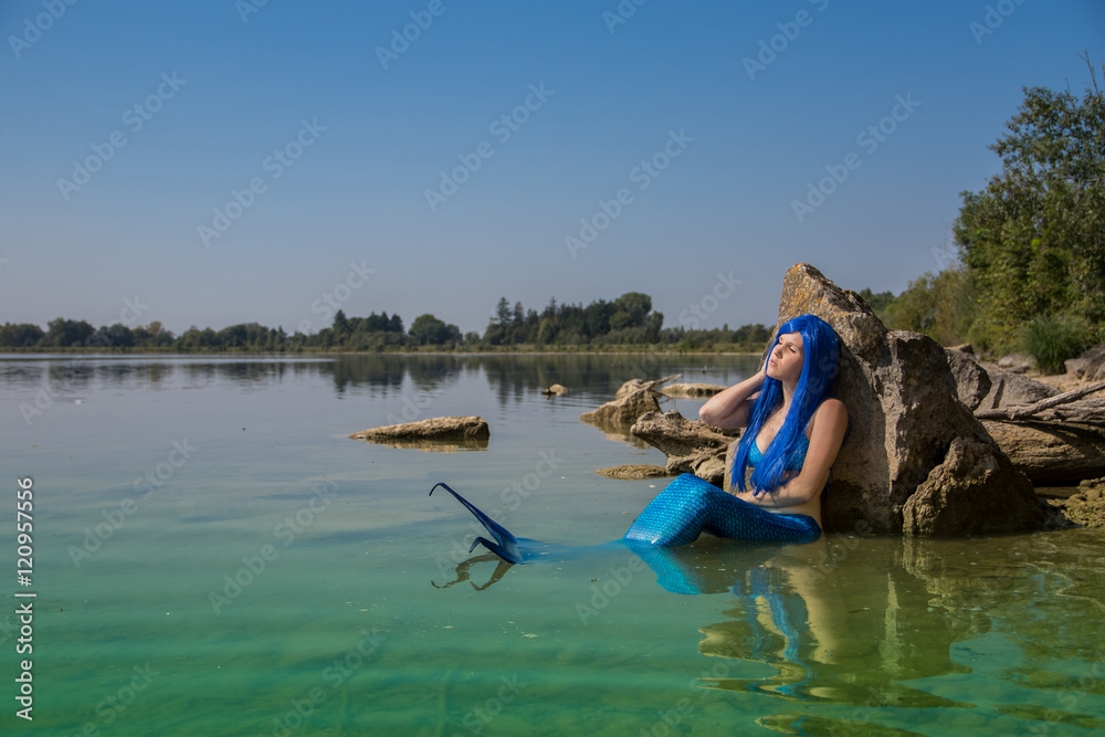 Meerjungfrau mit blauer Flosse am Ufer genießt Sonnenbad