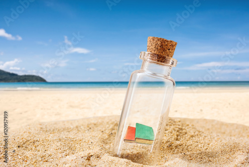 bottle with age book on sand beach over blue sea and sun light.