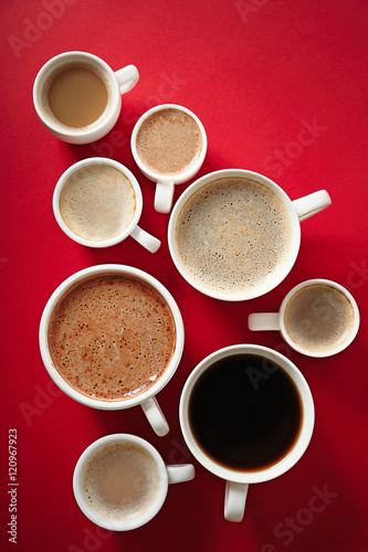 Cups of coffee on red background, top view