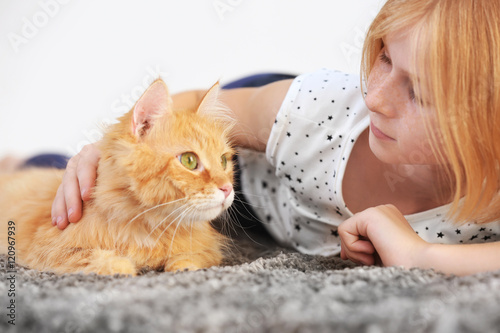 Beautiful little girl lying on floor with red fluffy cat