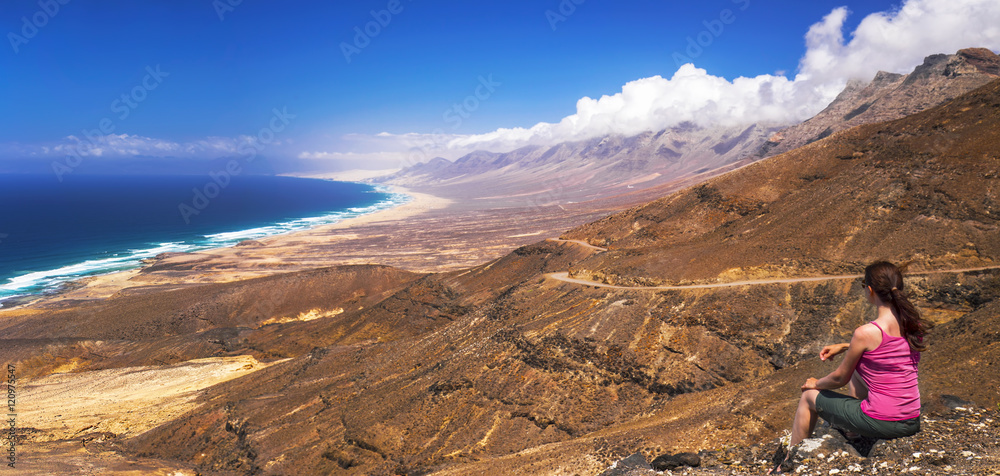 Young beautiful woman enjoying the view to Cofete sandy beach with vulcanic mountains in the background, Jandia,  Fuerteventura, second biggest Canary island, Spain.