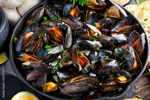Boiled mussels in iron pan cooking dish. with herbs, butter, lime, parsley, garlic and fresh bread.