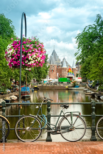 Typical Amsterdam view with bikes, canals and historical buildings. In the back, Nieuwmarkt square is dominated by the gate of the medieval city. © mandritoiu