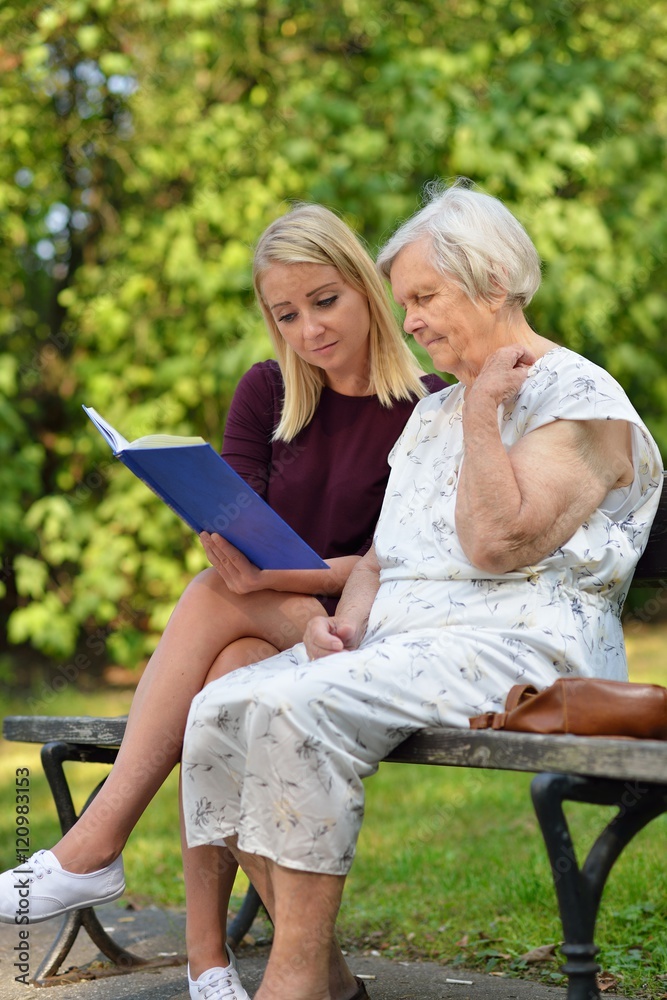 Young woman reading a book elderly woman in the park. Young woman reading a book elderly woman in the park.