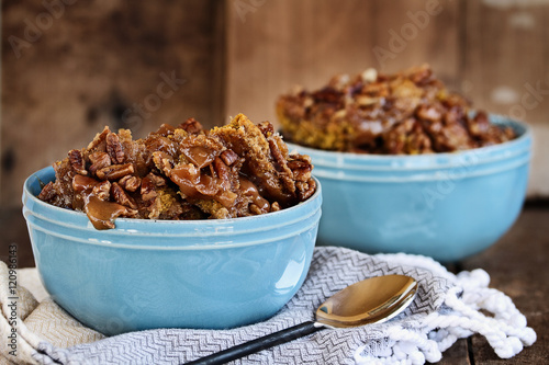 Hot autumn dessert pumpkin cobbler made with pumpkin spice and pecans against a dark rustic moody background. 