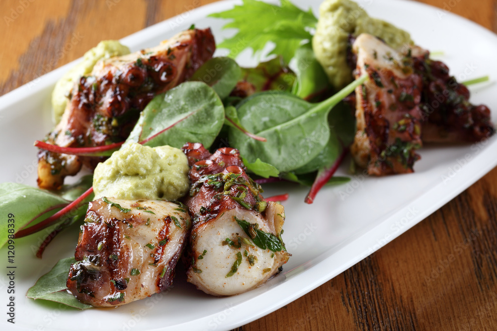 Grilled octopus with chili, sauce and herbs on white dish