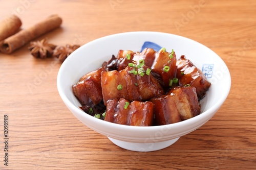 Stewed meat of pork in chinese style in white bowl in wooden tab