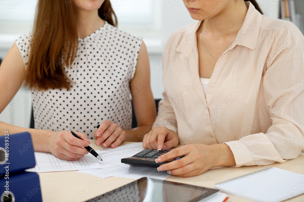 Two female accountants counting on calculator income for tax form completion hands closeup. Internal Revenue Service inspector checking financial document. Planning budget, audit concept Two female accountants counting on calculator income for tax form completion hands closeup. Internal Revenue Service inspector checking financial document. Planning budget, audit concept