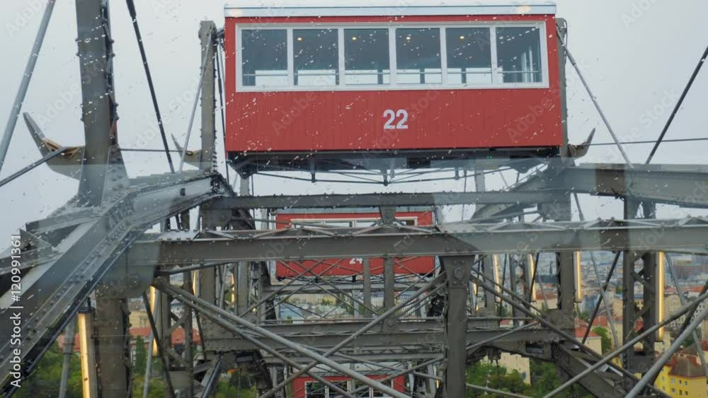 Ferris wheel with cabins moving up. View through the glass on rainy day ...