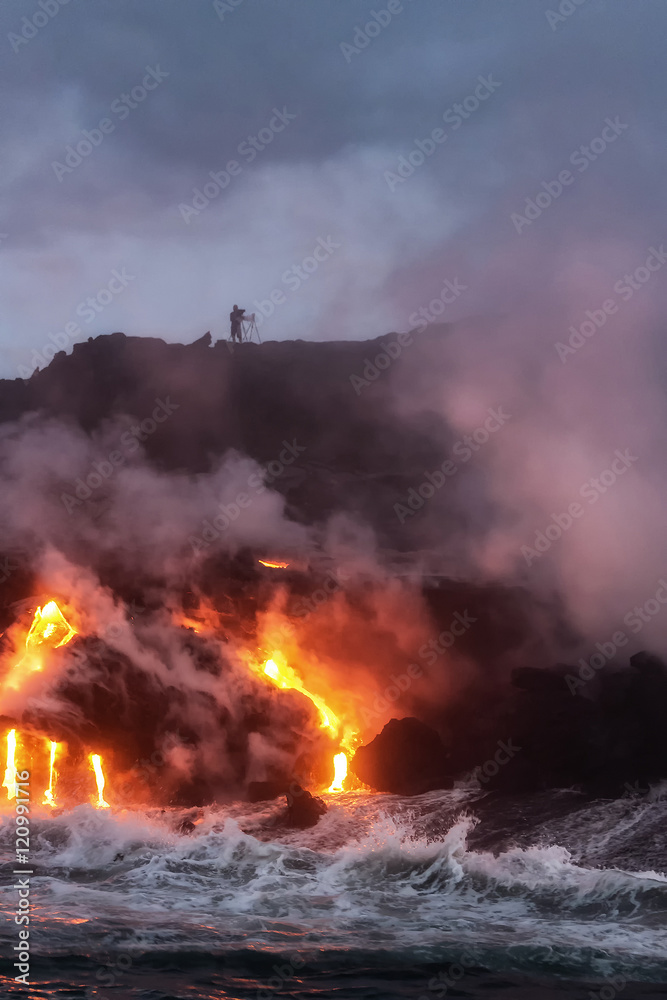 Molten lava from Kalapana lava flowing into Pacific Ocean early morning with silhouette of photographer on cliff