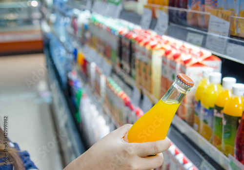 Woman holding a bottle of orange juice shelves at supermarket.