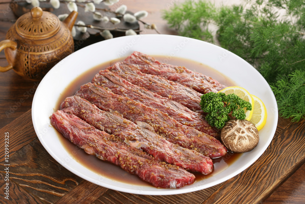 Seasoned sliced beef on white plate with lemon, mushroom and her Seasoned sliced beef on white plate with lemon, mushroom and her