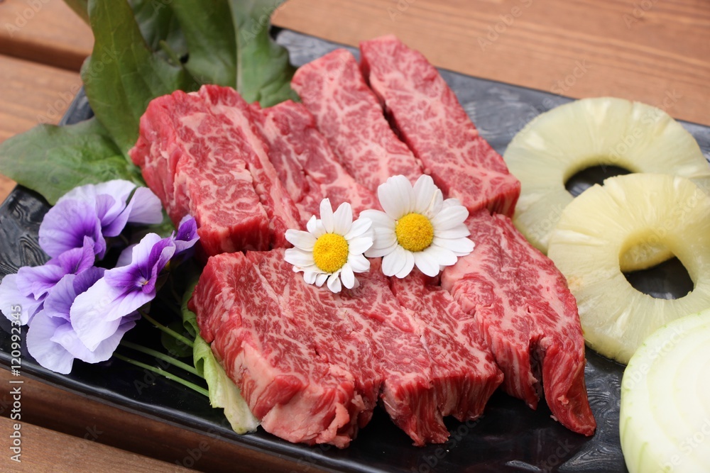 Fresh red beef with sliced pineapple and flowers on black plate Fresh red beef with sliced pineapple and flowers on black plate