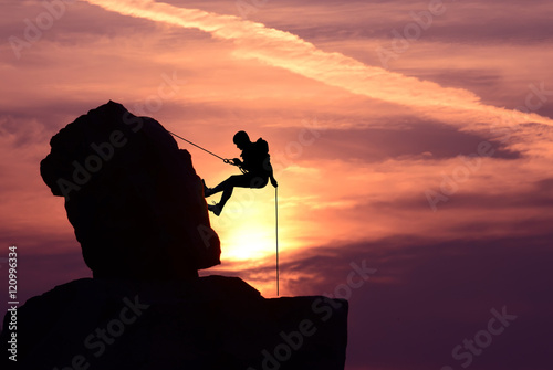 Man rock climber silhouette over bright sunset photo