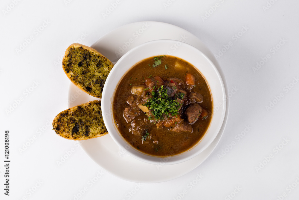 Poucher of Goulash soup with roasted toast and beef on white bac Poucher of Goulash soup with roasted toast and beef on white bac