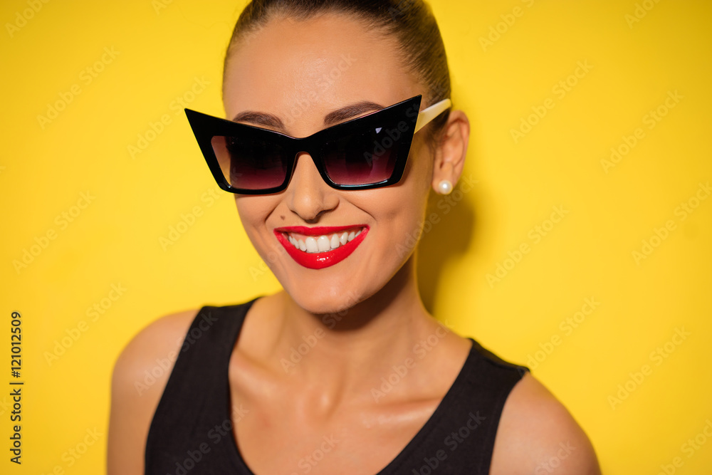 Elegance and style. Close up studio portrait of gorgeous young woman in sunglasses is smiling. Yellow background. Elegance and style. Close up studio portrait of gorgeous young woman in sunglasses is smiling. Yellow background.