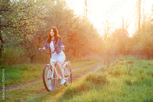 Week end in spring park. Attractive young brunette woman riding on bicycle against nature background.