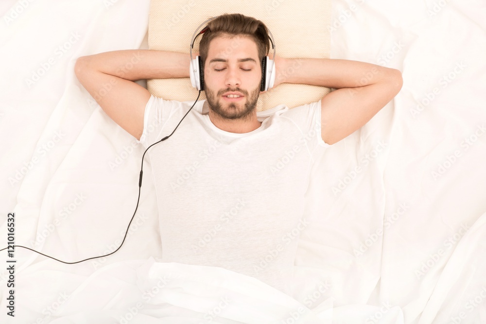 Portrait of a handsome man from above with headphones in bed.. Portrait of a handsome man from above with headphones in bed..