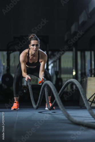 Concept: power, strength, healthy lifestyle, sport. Powerful attractive muscular woman CrossFit trainer do battle workout with ropes at the gym