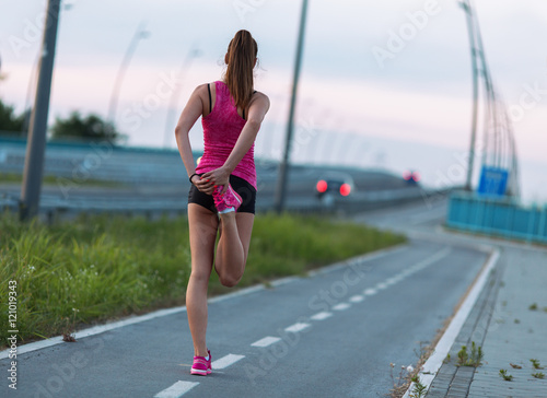 Young female in sports wear jogging on the street.She stretching her body and legs.