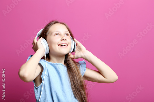 Portrait of young girl with headphones on pink background