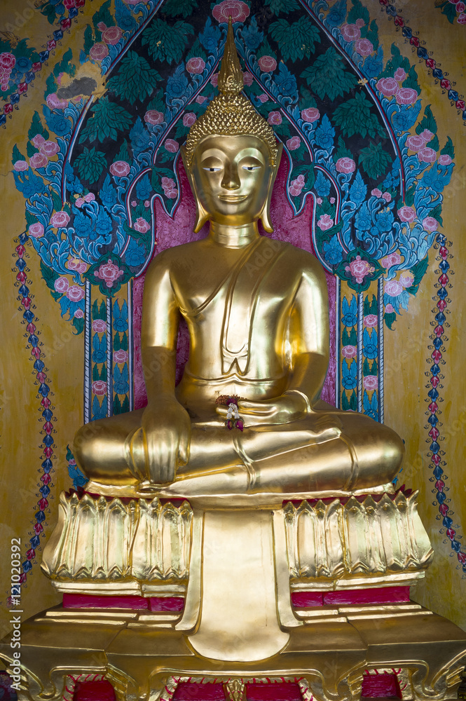 Golden buddha sits in fornt of a decorative floral patterned background in a Buddhist temple in Chiang Mai, Thailand