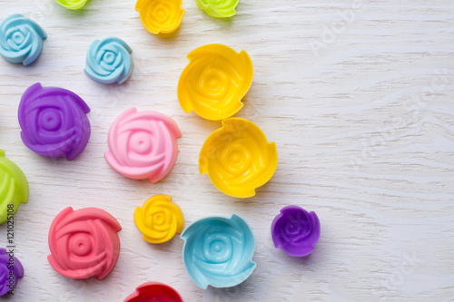 Colorful of silicone molds for baking in the form of flower on white wood.