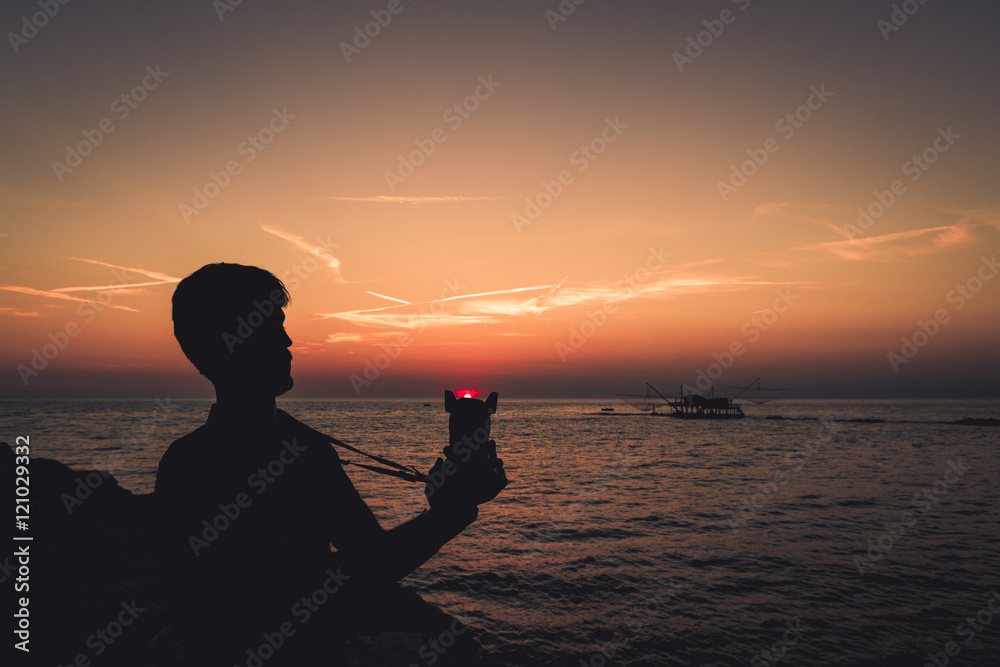 Fototapeta premium Silhouette di un ragazzo giovane che tiene in mano una macchina fotografica al tramonto.