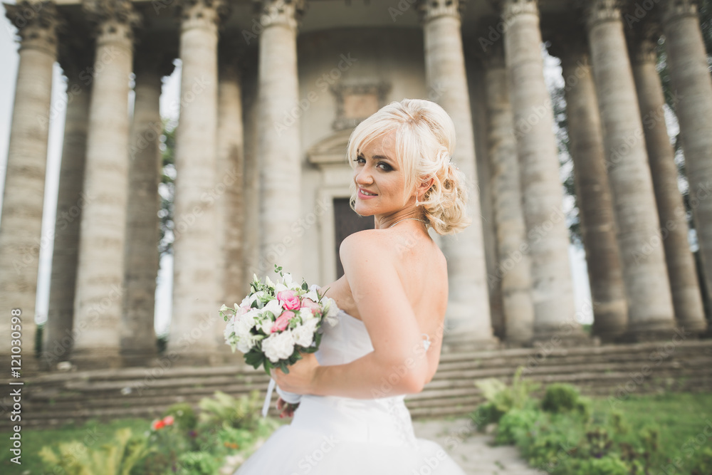 Beautiful elegant bride with perfect wedding dress and bouquet posing near old castle Beautiful elegant bride with perfect wedding dress and bouquet posing near old castle