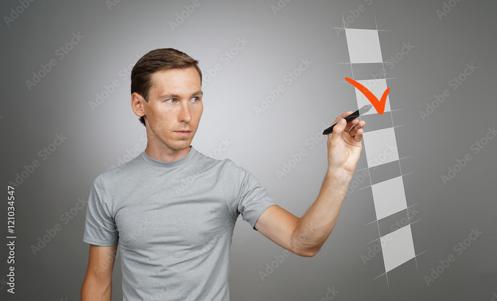 Young man in t-shirt checking on checklist box. Gray background. Young man in t-shirt checking on checklist box. Gray background.