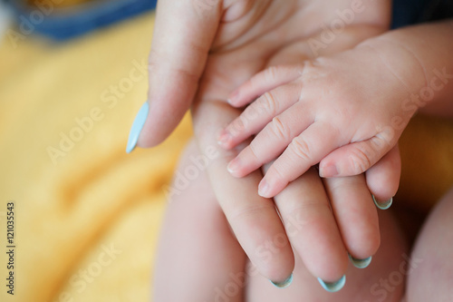 Newborn baby put his little hand on the palm of his gentle mother,the mother's nails are painted blue nail Polish,the baby and mother are sitting on soft yellow blanket